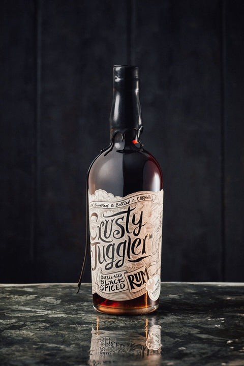 A bottle of Rusty Juggler Black Spiced Rum stands on a glass table.