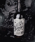 A dark glass bottle of Crusty Juggler Black Spiced Rum with a white label, set against a dark, glossy, water-rippled background.