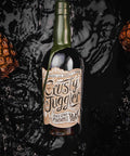 A bottle of Rusty Juggler Black Star Pineapple Rum centered against a glossy black liquid splash background with pineapple crown props on the sides.